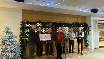 A giant cheque being held by two people with a small group in the background clapping