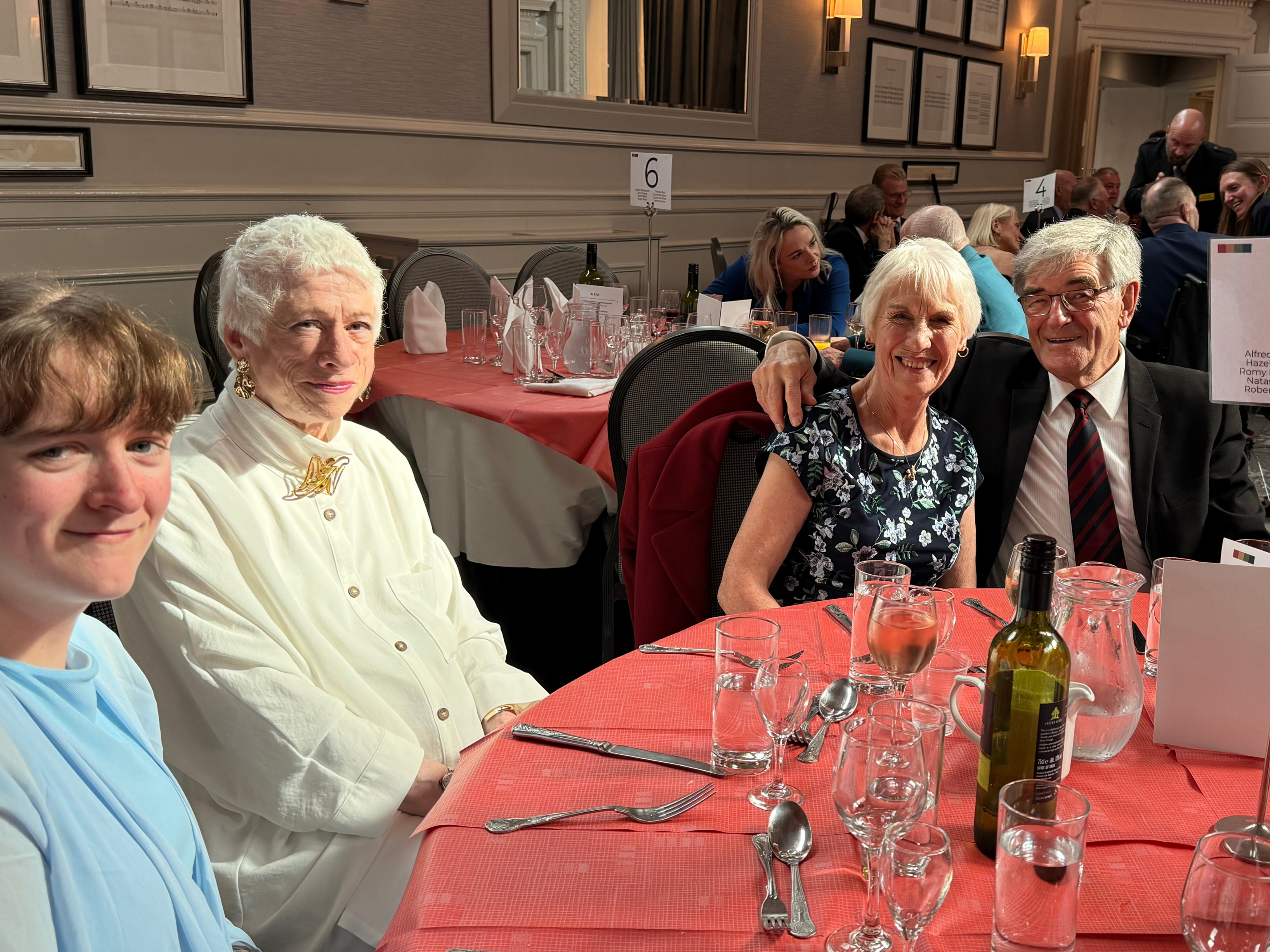 Guests are seated at a round table, smiling. 