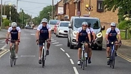 Five cyclists riding along next to each other across the width of the road