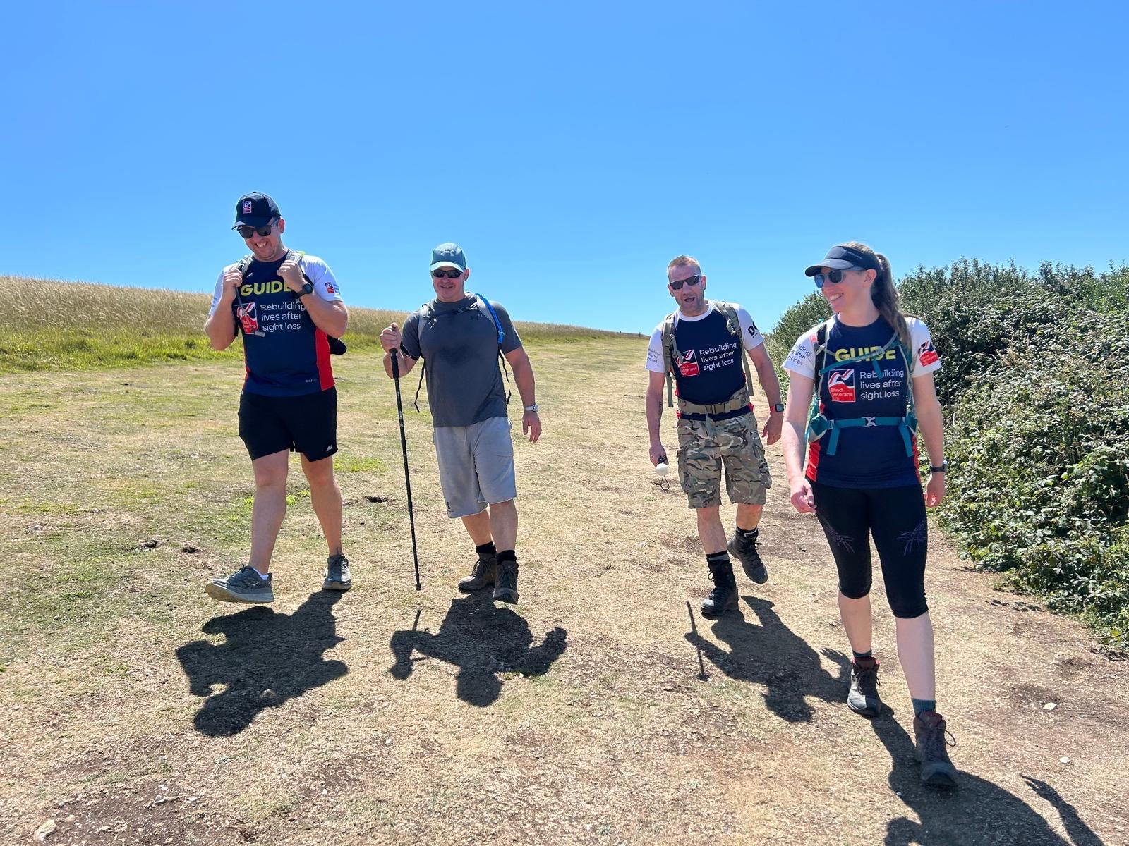 A group of four walk along the South Downs Way. Theresa and Rich are both wearing Blind Veterans UK T-shirts with 'Guide' written on the front and Stuart and Charlie walk with their white canes 