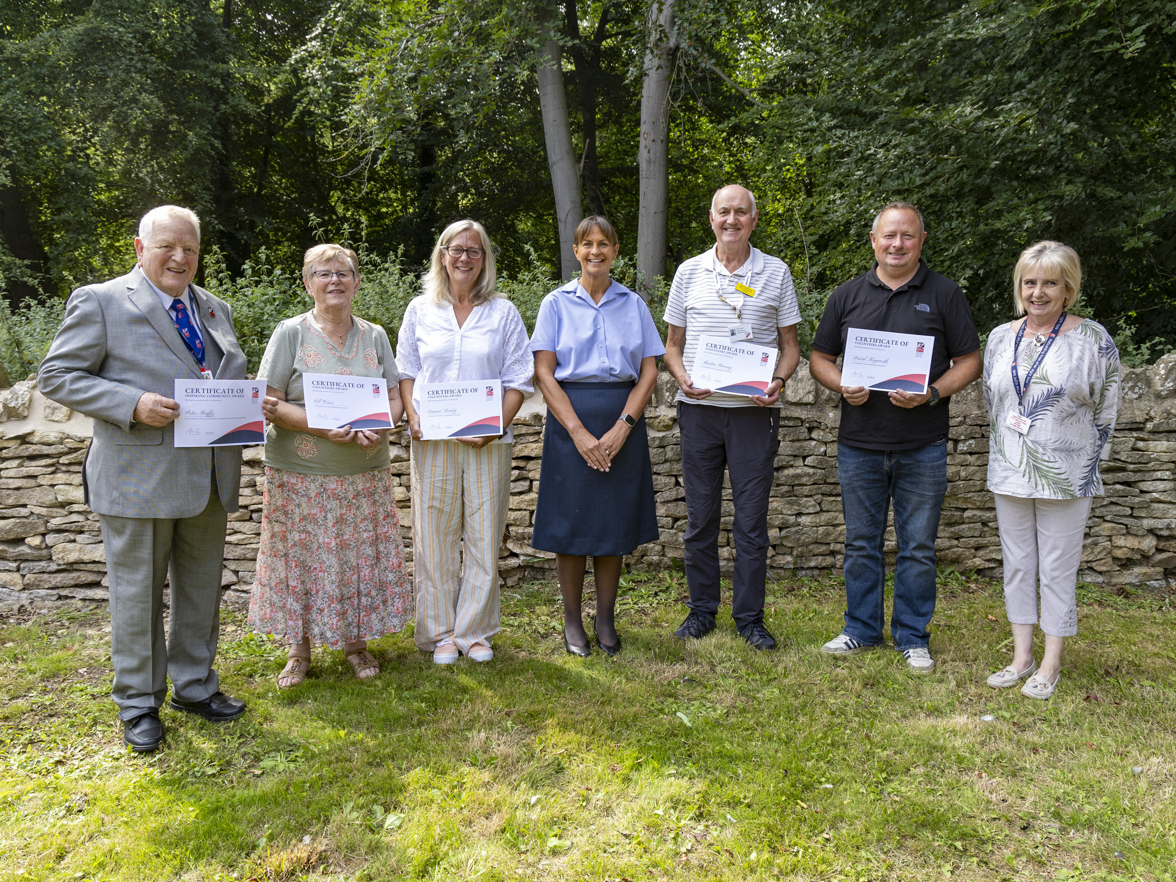 A group photographs of volunteers gathered together outside, smiling as they hold up their certificates.