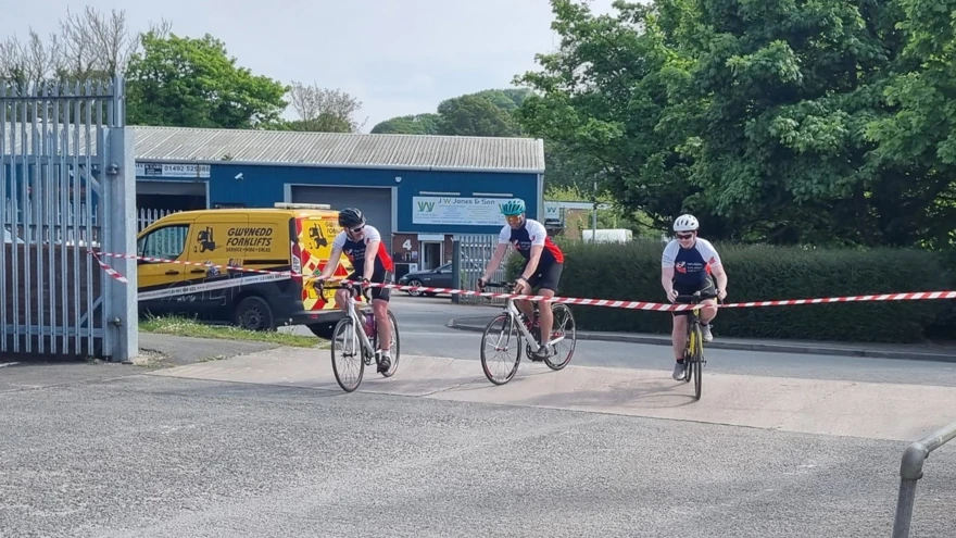The three cyclists just a metre away from the finish line tied across the gates at their place of work