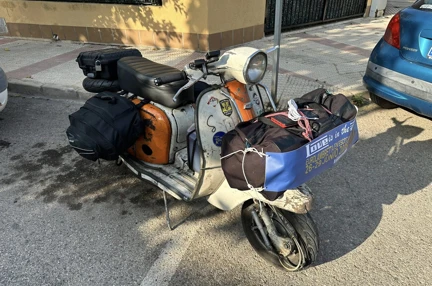 Orange and white 1970s Lambretta scooter with bags tied to the front and either side of the seat
