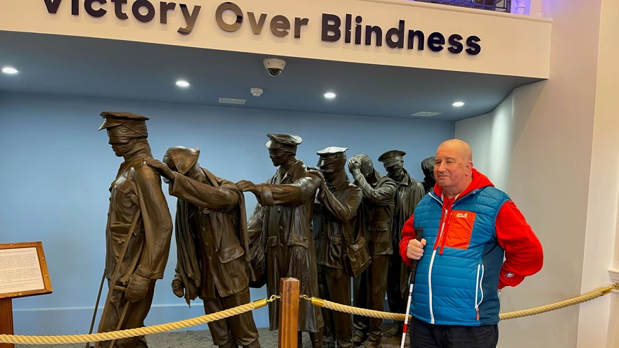 Blind veteran John standing with his white cane, in front of our Victory Over Blindness statue