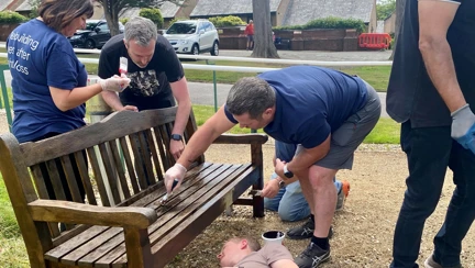 Four Thea colleagues working together to varnish a wooden garden bench at our Blind Veterans UK Llandudno Centre of Wellbeing. One of the group is lay on the floor so he can reach underneath.