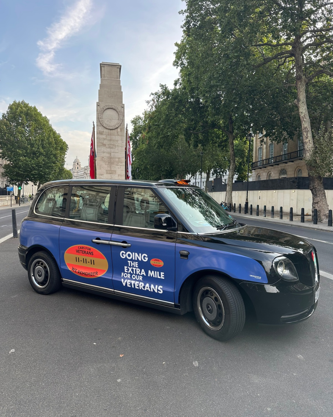 A blue and black Cabs for Veterans taxi parked beside the Cenotaph in London. Text on the taxi reads, “Going the extra mile for our veterans.”
