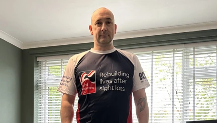 Blind veteran Steve standing in his living room wearing his Blind Veterans UK t-shirt