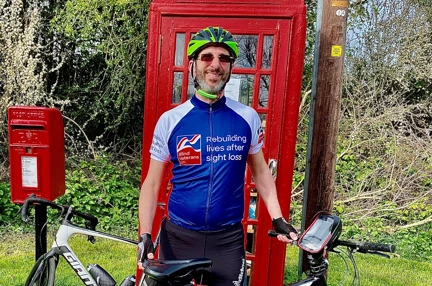 Rob wearing a Blind Veterans UK cycling top stood with his bicycle in front of a red telephone box