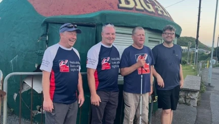 A group shot of the four men during the challenge. Stood in front of a kiosk that looks like a large apple.