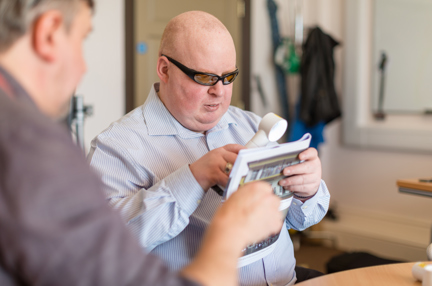 Karl Poole reading using specialised glasses and a magnifying glass at the Llandudno centre