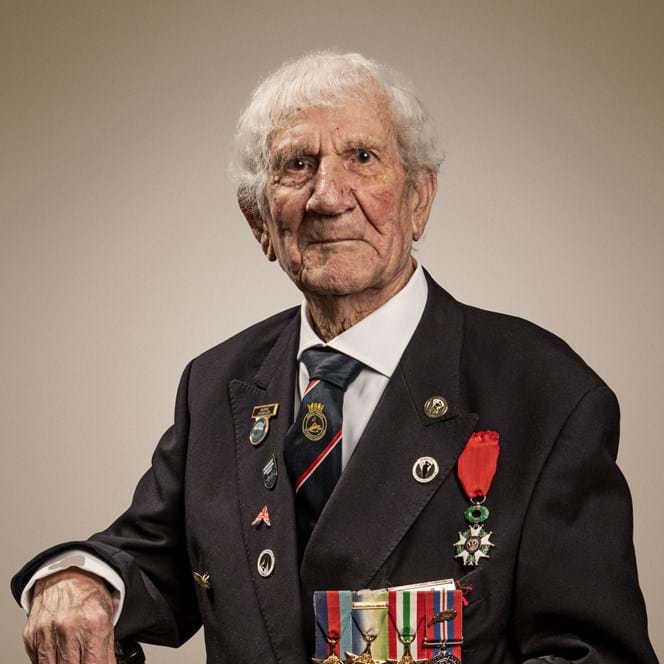 Blind veteran George in a suit wearing his medals and sitting in a chair