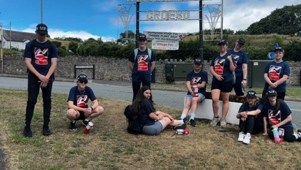 A group of police cadets resting on the grass by the 'Llandudno Welcomes You' sign.