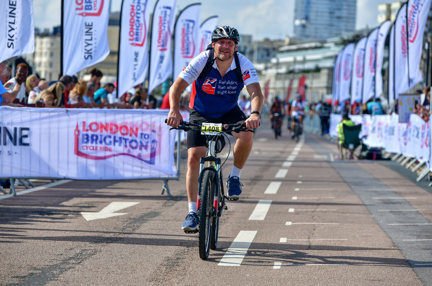 Gary crossing the finish line of the race on his bike wearing a Blind Veterans UK t shirt.