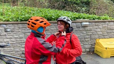 Sheila being helped to put on her cycling helmet by a member of charity staff