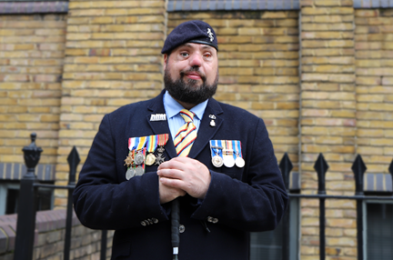 Blind veteran Simon, smiling and wearing his military uniform with badges and a beret