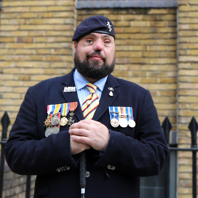 Blind veteran Simon, smiling and wearing his military uniform with badges and a beret