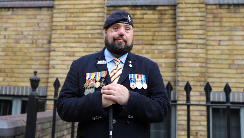 Blind veteran Simon, smiling and wearing his military uniform with badges and a beret