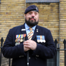 Blind veteran Simon, smiling and wearing his military uniform with badges and a beret