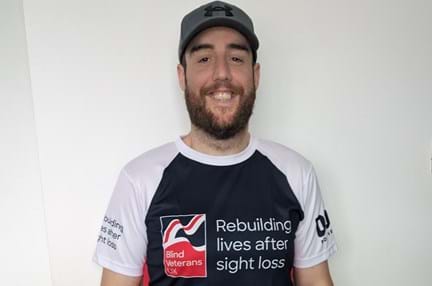 Chris stood inside in his Blind Veterans UK running top and a baseball cap with a huge smile on his face