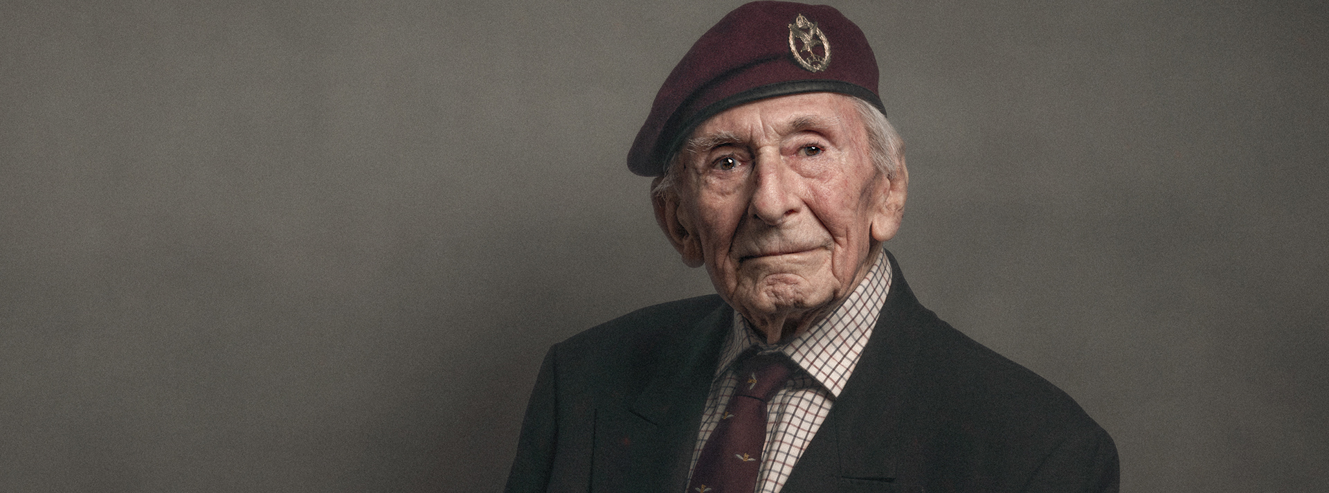A close-up of blind veteran Jim, wearing a maroon beret with a suit and tie