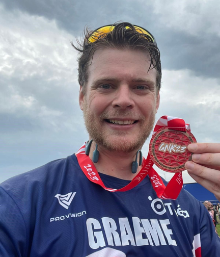 A flushed but happy looking Graeme holds his medal up as he smiles for the camera.