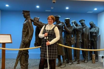 Blind veteran Sheila stood holding her came in front of the Victory over Blindness Statue at the Llandudno Centre