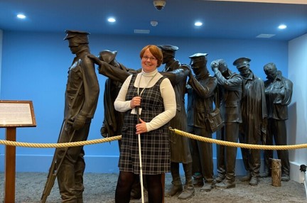 Blind veteran Sheila stood holding her came in front of the Victory over Blindness Statue at the Llandudno Centre