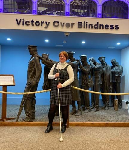 Blind veteran Sheila stood holding her came in front of the Victory over Blindness Statue at the Llandudno Centre