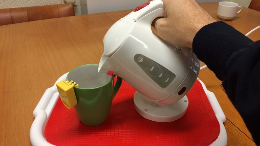 A yellow liquid level indicator attached to the side of a mug, as a hand pours hot water from a kettle