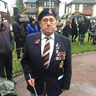 Bob is wearing a poppy and medals and looks into the camera. He is holding his guide cane.