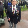 Bob is wearing a poppy and medals and looks into the camera. He is holding his guide cane.