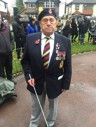 Bob is wearing a poppy and medals and looks into the camera. He is holding his guide cane.
