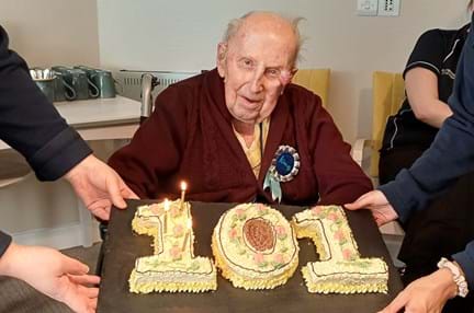 Ken looks at the camera with his very special cake in the shape of the number 101 in front of him