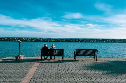 A photo of two older people sitting on a bench at the seafront
