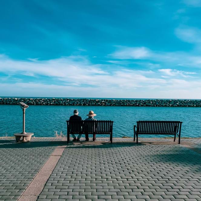 A photo of two older people sitting on a bench at the seafront