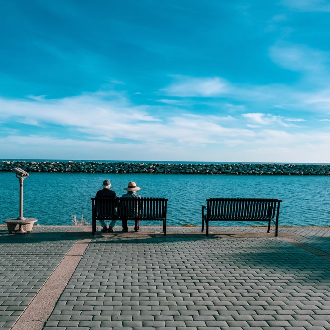 A photo of two older people sitting on a bench at the seafront