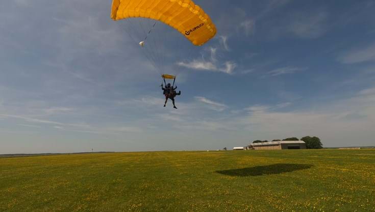 Mark and his tandem instructor approaching the ground and getting into position for the landing with yellow open parachute above them