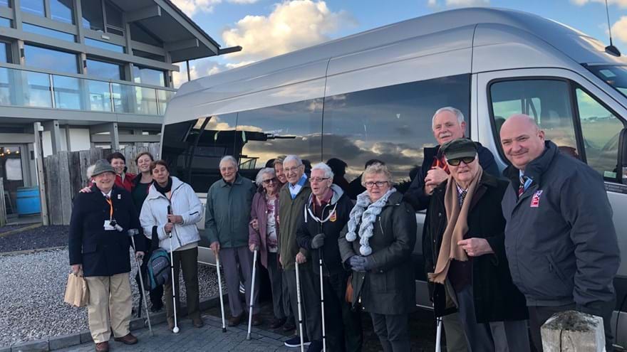 A photo of a group of blind veterans and staff gathered together in front their transport van as they arrived at Quay Hotel & Spa in Deganwy for afternoon tea