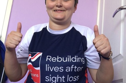 Laura pictured smiling and putting her thumbs up, wearing a Blind Veterans UK top