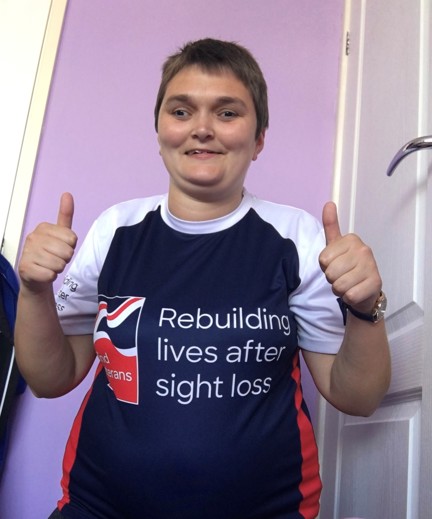 Laura pictured smiling and putting her thumbs up, wearing a Blind Veterans UK top