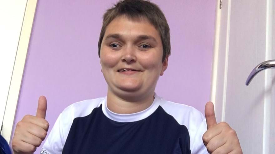 Laura pictured smiling and putting her thumbs up, wearing a Blind Veterans UK top