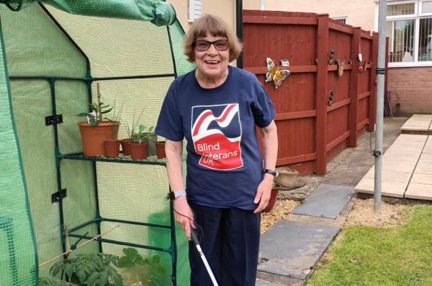 Noeline wearing Blind Veterans UK t-shirt stood in her garden holding her cane