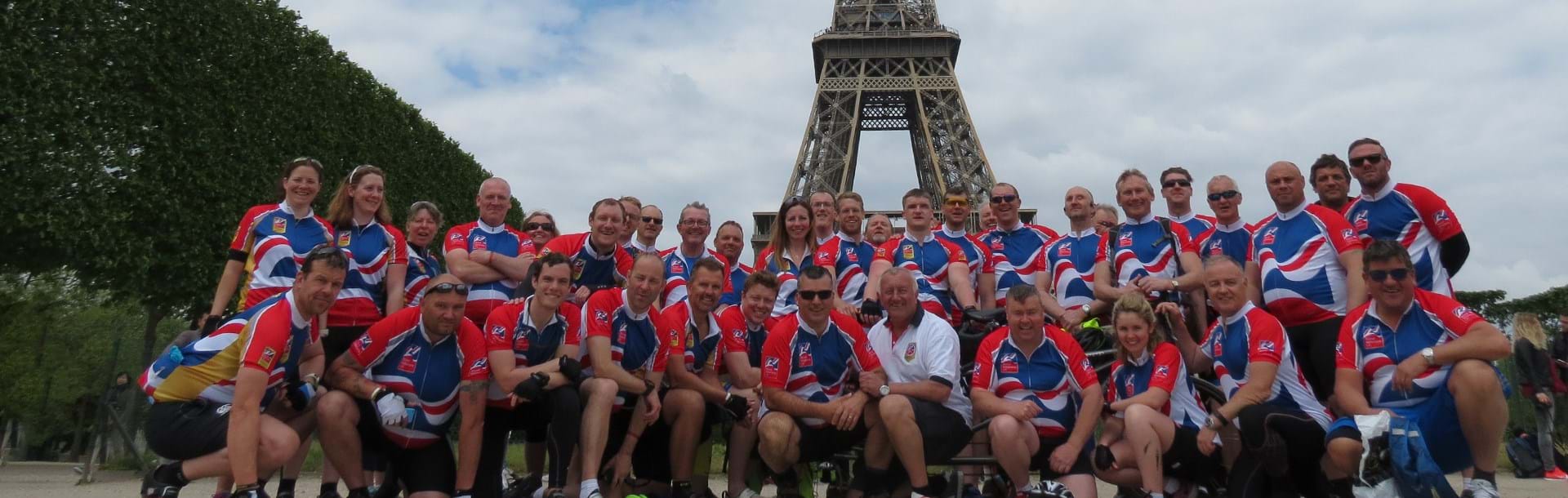 A  large group of blind veterans and charity supporters wearing Blind Veteran UK cycling vests as they pose in front of the Eiffel Tower