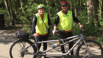 Richard and Maria dressed in high vis tops stood holding up their tandem bike