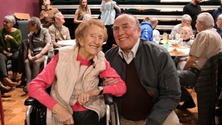 Blind veterans Margaret and Simon smiling and linking arms at her birthday party