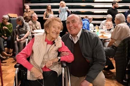 Blind veterans Margaret and Simon smiling and linking arms at her birthday party