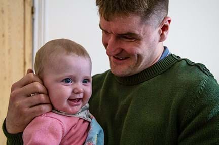 Blind veteran Rob smiling and holding his baby daughter who is giggling