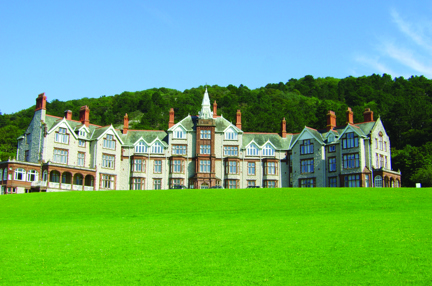 Our Llandudno Centre of Wellbeing building on a sunny day, with tall trees in the background and well kept grass at the entrance