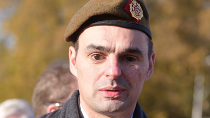 Craig dressed in a black coat with a poppy in his button hole and wearing a beret
