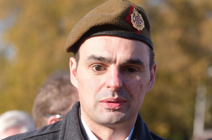 Craig dressed in a black coat with a poppy in his button hole and wearing a beret